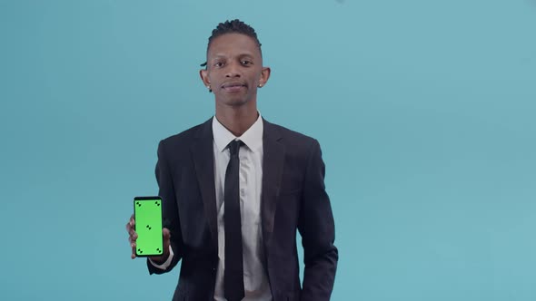 Black Male Businessman in a Strict Office Suit Holds a Phone with an App and Smiles Positively Nods