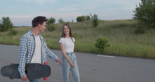 Couple of Teens Talking Having Joy and Laughing During Walk with Skateboard