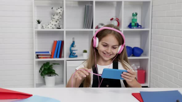 Happy Amazed Child in Modern Headphones Watching Video on Smartphone in Classroom Modern Education