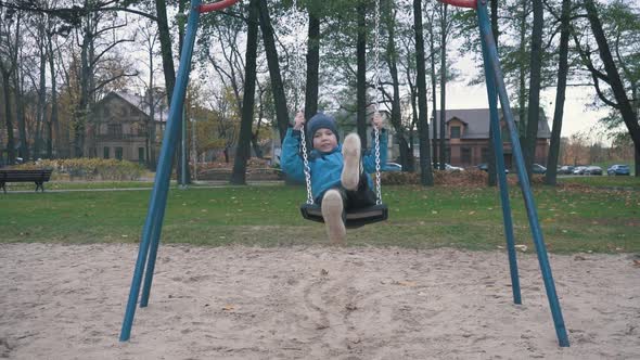 Boy is Swaying on Swing in Park at Autumn Day and Jumping Out in Slow Motion