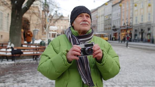 Senior Old Man Taking Pictures with Photo Camera Smiling Using Retro Device in Winter City Center