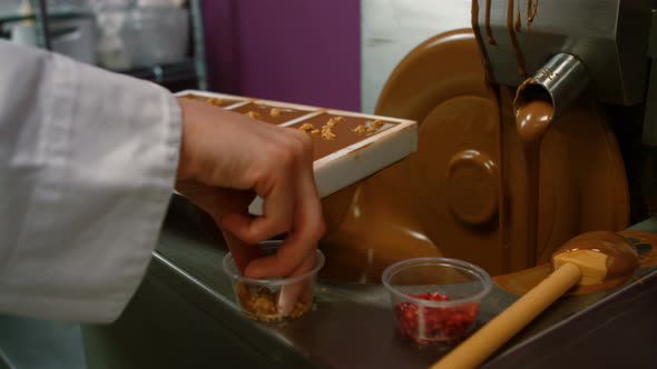 Worker sprinkling nuts on top of melted chocolate