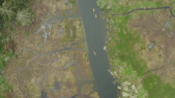 Far away top down drone shot of a canoe and two kayaks being paddled through an estuary