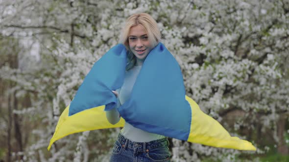 Female Blonde with Ukrainian Flag Posing in Blossoming Park