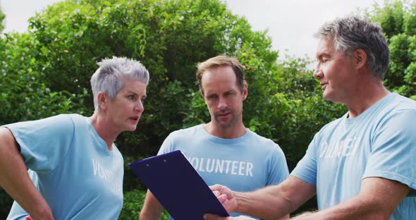 Caucasian senior couple with clipboard and man wearing volunteer t shirts talking in field