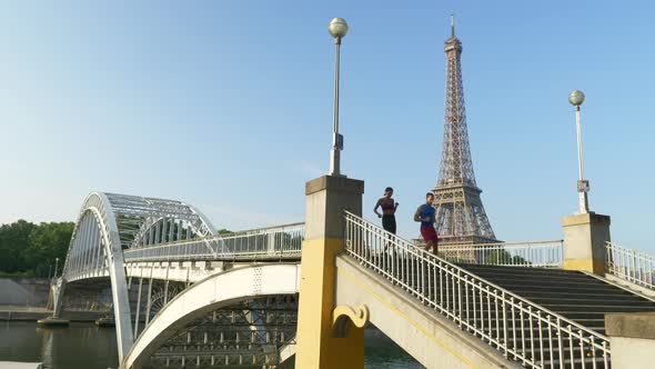 A man woman couple running across a bridge with the Eiffel Tower