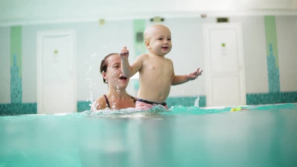 Young Mother is Lifting Her Son From the Water Holding His Feet While Teaching Him How to Swim in