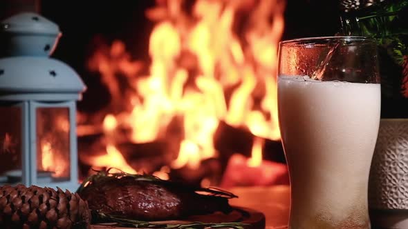 Cold beer poured from bottle glass on background of burning fireplace