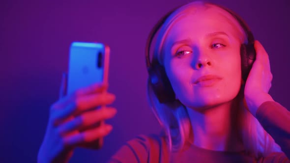 Young Beautiful Fashionable Girl Uses a Smartphone in a Bar or Club on Background of Neon Lights