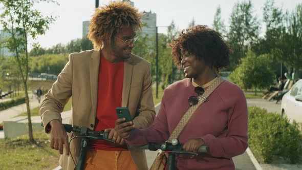 Afro Friends Standing with E-Scooters in Park and Chatting