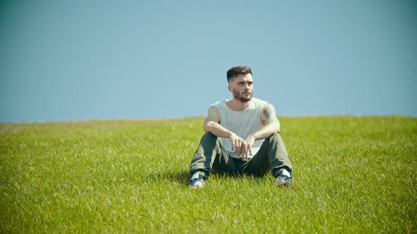 A Young Man with Tattoos Sitting on a Bright Green Grass