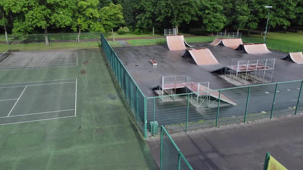 Aerial view flying above fenced skateboarding basketball and tennis court in empty closed playground