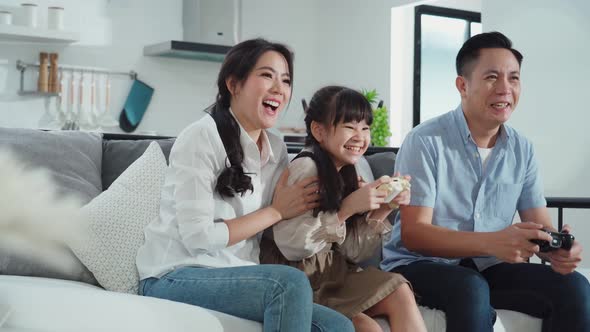 Asian family kid, mother, father playing mobile game on smartphone together in living room at home.