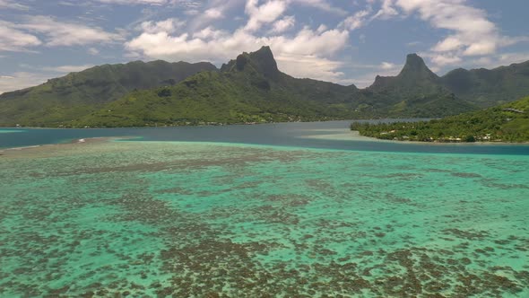 Aerial establishing shot of Mo'orea island, flying over the barrier reef and stunning mountains on b