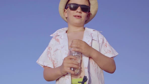 Boy in Sunglasses Unscrews the Cork of a Water Bottle and Drinks Water