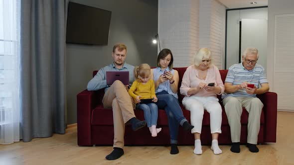 Family Goes and Sits on the Couch with Personal Gadgets. Addicted To Modern Technology Phone Devices