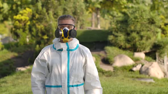 Portrait Young Man in a Protective Suit, Glasses, a Respirator and Gloves Holds a Smartphone with