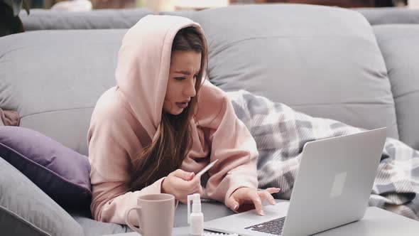 The Woman with Thermometer Is Lying in Bed and Looking for Symptoms in Laptop