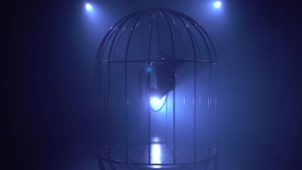 Girl in the Cage Performs Gymnastic Stunts in a Dark Room