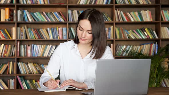 Attractive Lady Writes in Notebook at Videocall on Laptop