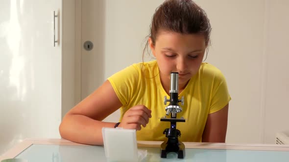 A Cute Teenage Girl in Yellow Tshirt is Looking Look Through the Microscope