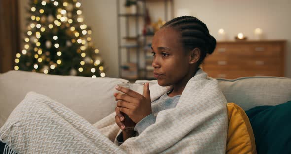 An Attractive Girl of African Appearance Covered with Blanket and Sitting on Couch