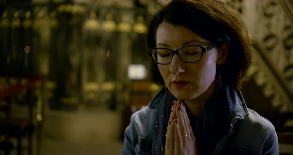 Calm Lady in Glasses and Denim Jacket Prays with Closed Eyes