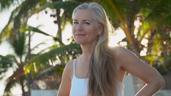 Serene mature woman smiles at camera and then nods her head yes and then looks to sky with palm tree