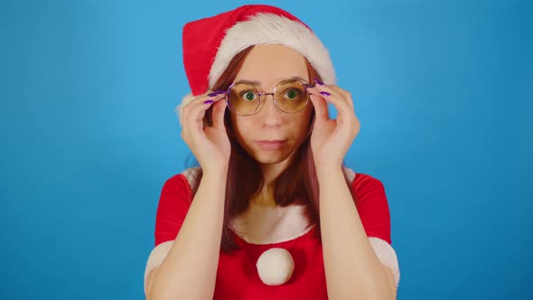 Woman in Santa Costume Adjusts Her Glasses Standing on Blue Background