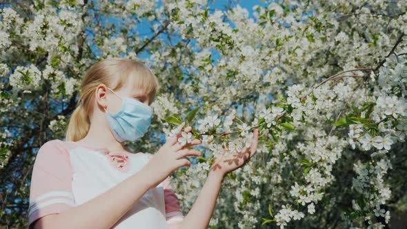 A Child Allergy Sufferer in a Mask Admires the Flowers on the Tree