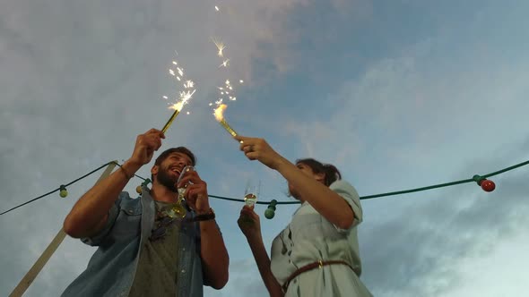 Under view of couple drinking champagne and waving with firework candles