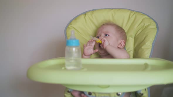 Mother Gives Spoon to Little Son Sitting in Green Highchair