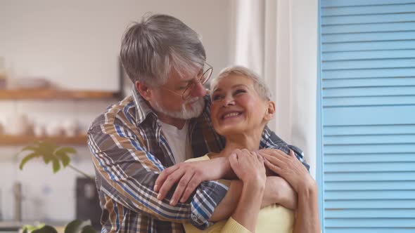 Mature Couple Hugging and Looking Out Through Window at Home