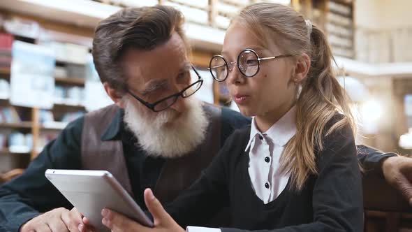 Grandfather with Glasses Talking with His Smiling Teen Granddaughter and Using Ebook