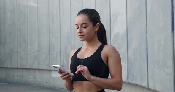 Sporty Young Woman Using Mobile Phone Outdoors After Jogging