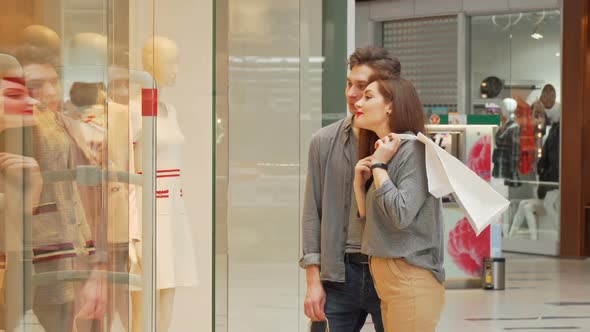 Happy Young Couple Shopping Together Examining Clothes on the Display of a Store