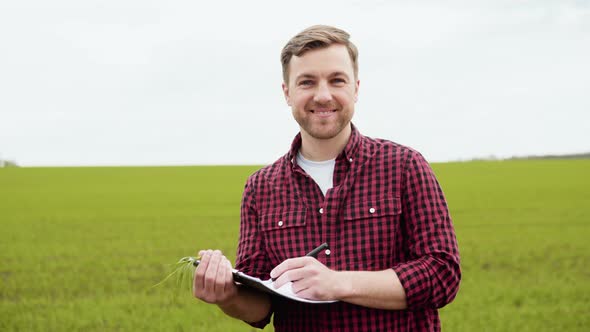 Portrait Shot of Attractive Farmer Standing in Green Field with Green Wheat and Notebook in the