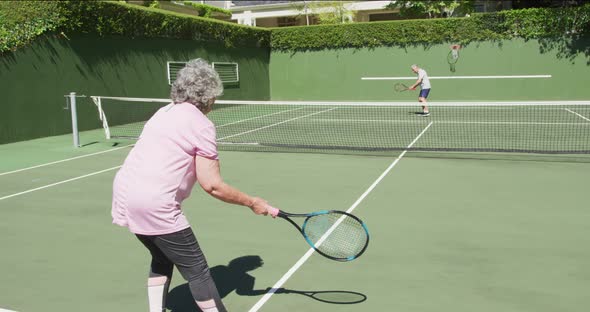 Caucasian senior couple paying a game of tennis on an outdoor court in the sun