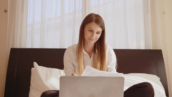 Woman Sitting with Laptop and Documents at Hotel Room