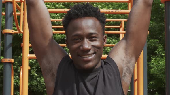 Sporty Black Guy Hanging On A PullUp Bar Exercising Outdoor