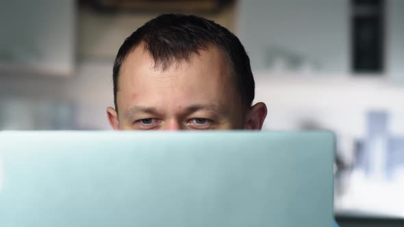 Man in surprise raises his eyebrows, reads news on the Internet in his laptop