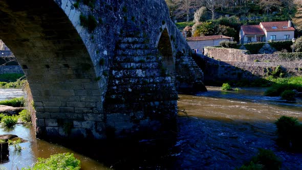 Aerial View Of Stone Arches Of Bridge of Ponte Maceira Over The River Tambre. Dolly Back