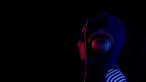 Profile of Teenager in Hoodie Sunglasses and Headphones in Darkness