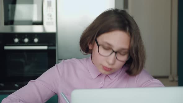 Close Up Portrain Schoolgirl in Glasses Teaches Lessons While at Home Sitting in the Kitchen at the