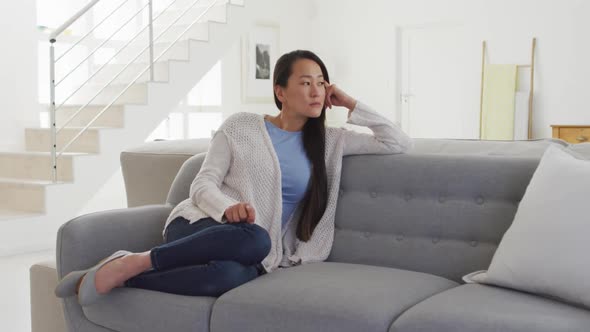 Thoughtful asian woman sitting at sofa at home