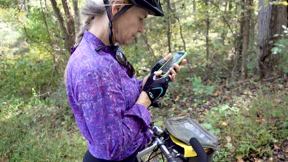 Mature woman wearing biking helmet and gloves outside checking her smartphone.