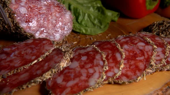 Panorama of Delicious Dry Sausage in Herbs Taken From a Wooden Board with a Fork