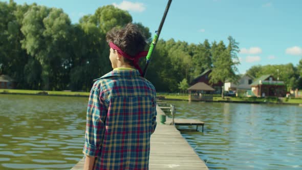 Rear View of Teenage Fisherman with Rod and Tackle Box Walking on Pier on Lake