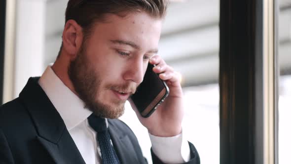 Serious Smartly Dressed Man Talking By Phone and Working at Cafe