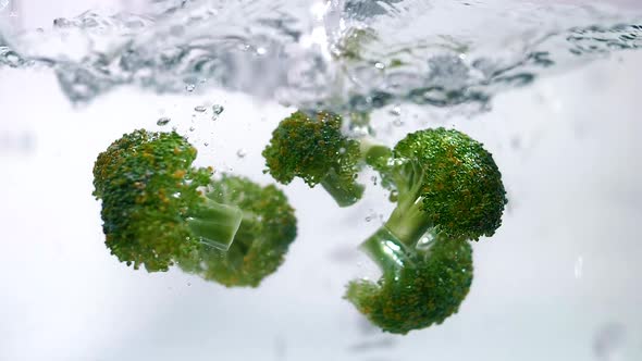 Fresh Green Broccoli Immersed in Clear Water in Slow Motion, White Background